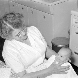 Older woman holding an infant in a kitchen.