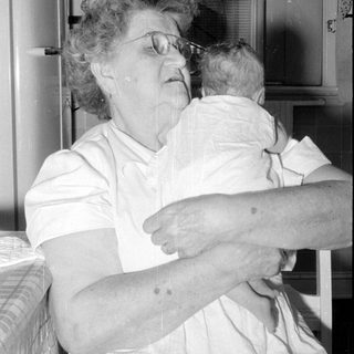 Woman with glasses holding an infant indoors.