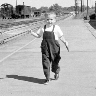 Boy in overalls on a train platform.