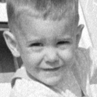 Child in overalls standing by TWA aircraft stairs.