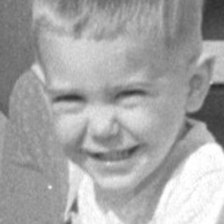 Child leaning over railing near TWA signage.