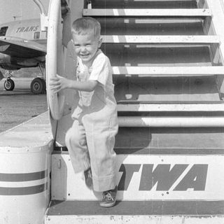 Child leaning over railing near TWA signage.