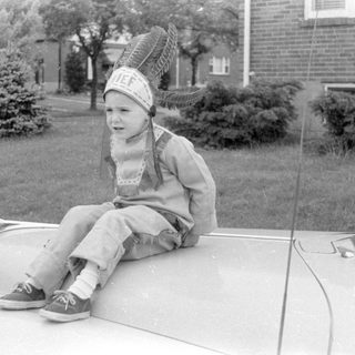 Child in headdress on car hood