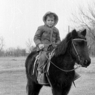 Child riding pony on paved road