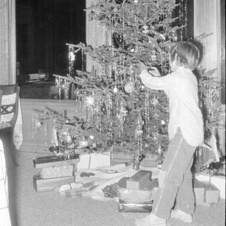Child decorating a Christmas tree with gifts