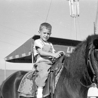 Boy in overalls sitting on a horse.