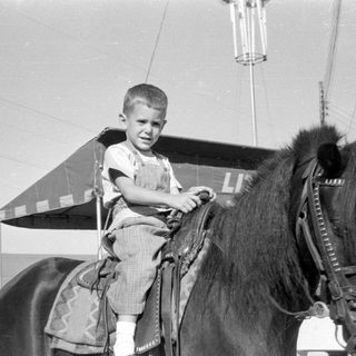 Boy in overalls sitting on a horse.
