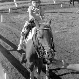 Child riding a pony in an outdoor arena.