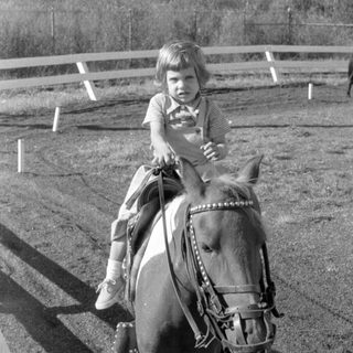 Child riding a pony in an outdoor arena.