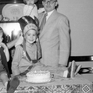 Family group with child in headdress and cake.