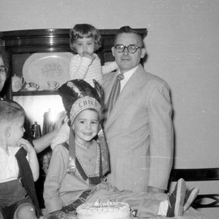 Family group with child in headdress and cake.