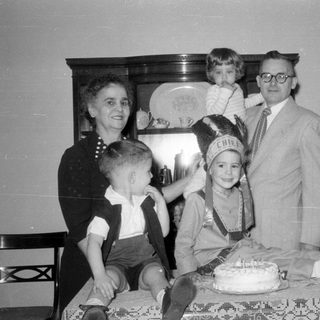 Family group with child in headdress and cake.