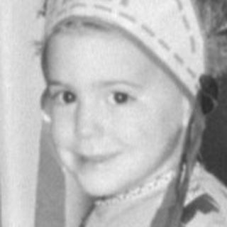 Child in headdress sitting by a birthday cake.