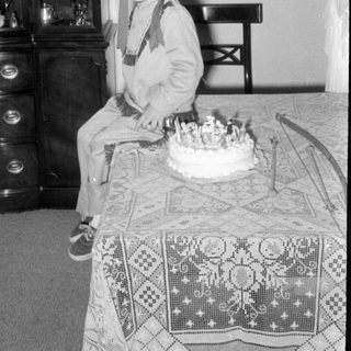 Child in headdress sitting by a birthday cake.