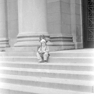 Child in headdress sitting on stone steps.