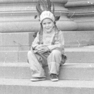 Child in headdress sitting on stone steps.