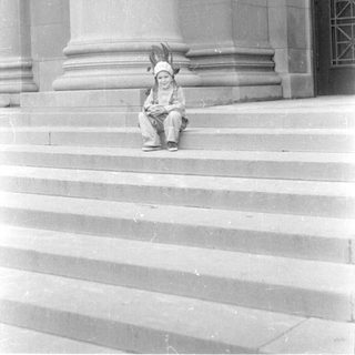 Child in headdress sitting on stone steps.