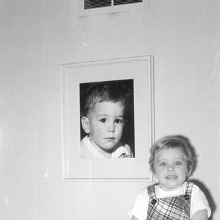 Child sitting next to a framed portrait.