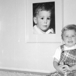 Child sitting next to a framed portrait.