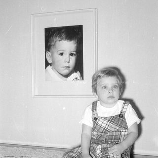 Child standing beside a framed portrait of a child.
