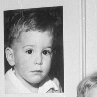Child standing beside a framed portrait of a child.