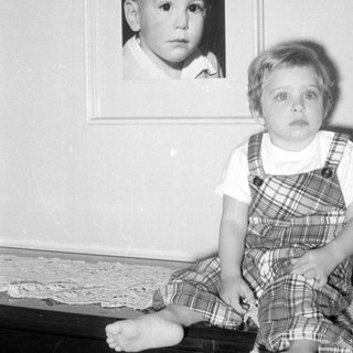 Child standing beside a framed portrait of a child.