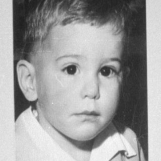 Child standing beside a framed portrait of a child.