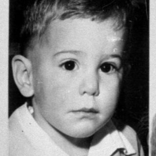 Child posing next to a framed baby portrait.