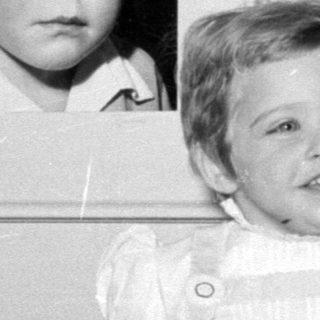 Child posing next to a framed baby portrait.