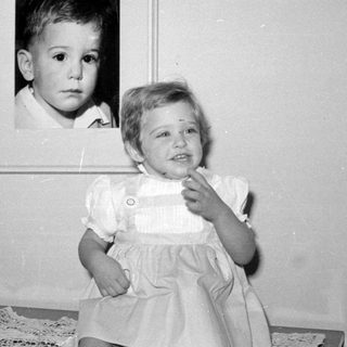 Child posing next to a framed baby portrait.