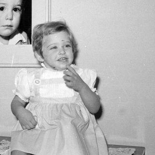 Child posing next to a framed baby portrait.