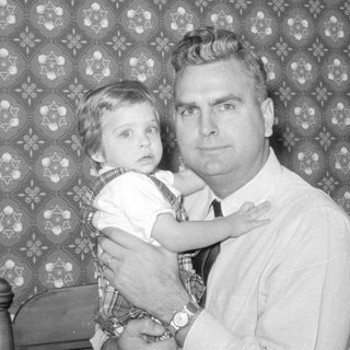 Man and young child against patterned wallpaper.