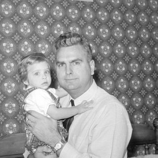 Man and young child against patterned wallpaper.