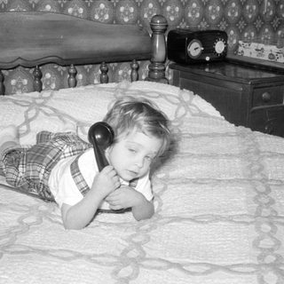 Child lying on a bed using a rotary phone.