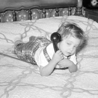 Child lying on a bed using a rotary phone.