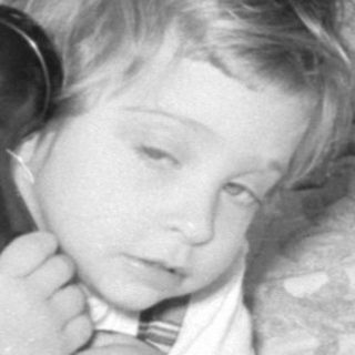 Child lying on a bed using a rotary phone.