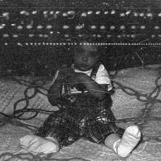 Infant in plaid trousers on patterned fabric.