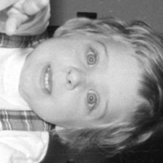 Child in plaid dress looking through crib bars.