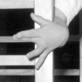 Child in plaid dress looking through crib bars.