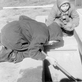Two children by a concrete opening outdoors.