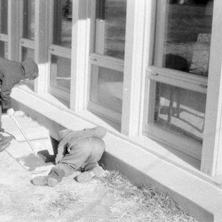 Two people working outside a windowed building.