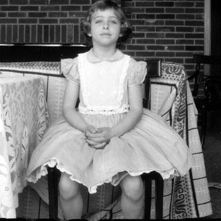 Young girl in a lace apron before brick wall.