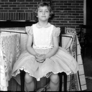 Young girl in a lace apron before brick wall.