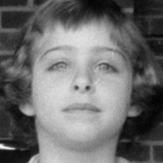 Young girl in a lace apron before brick wall.