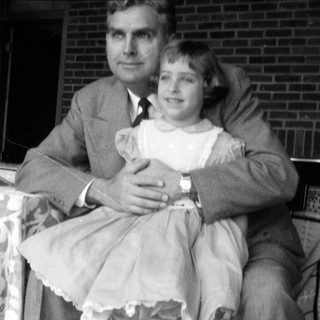 Man in suit and girl in dress outdoors.