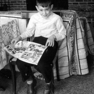 Boy holding a magazine in front of a fireplace.