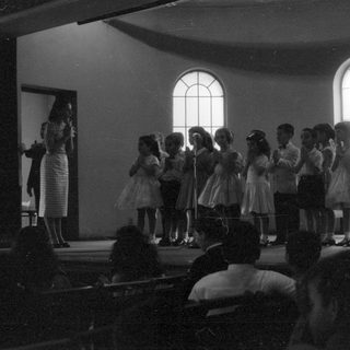 Children performing on a stage in a hall.