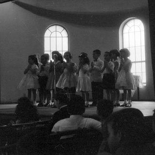 Children performing on a stage in a hall.