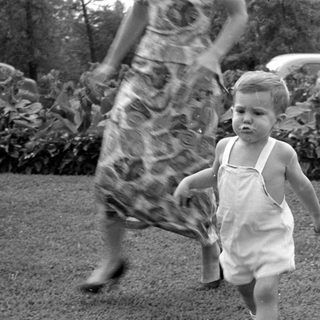 Toddler in white overalls walking on a lawn.
