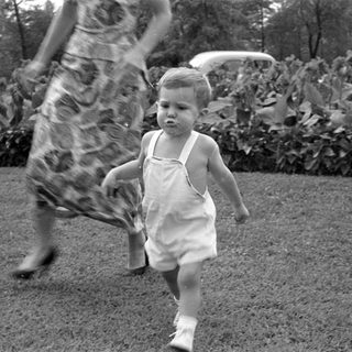Toddler in white overalls walking on a lawn.